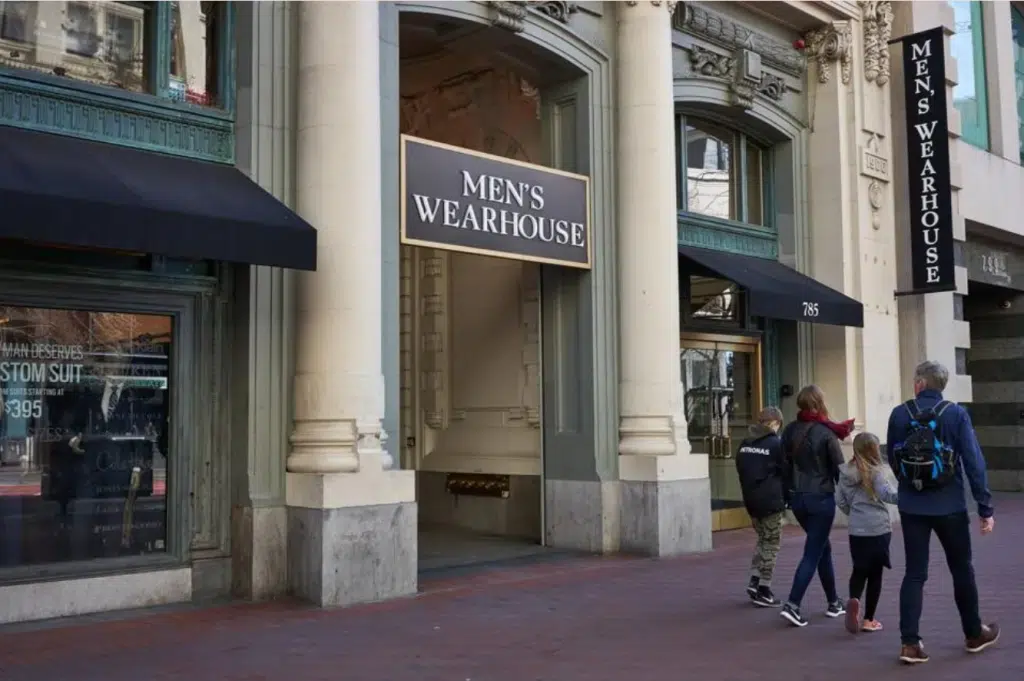Three people walking in front of a Men's Wearhouse storefront